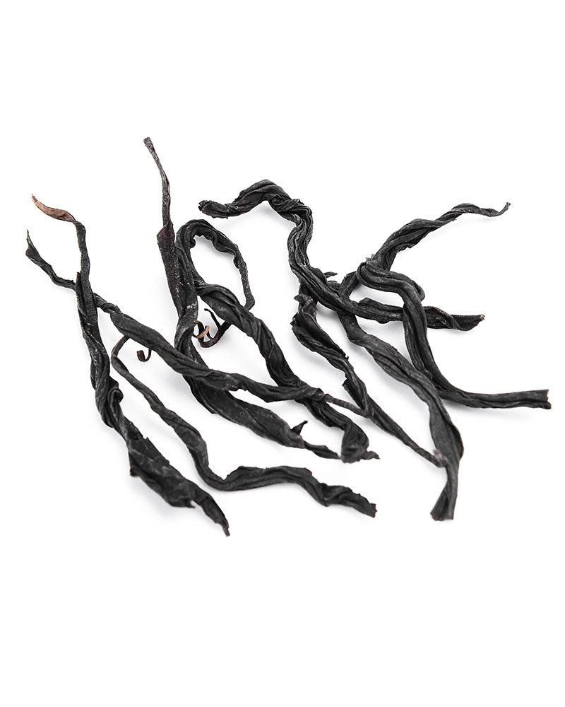 A group of dry, black seaweed strands are scattered on a white background, reminiscent of the intricate threads found in Wild Red Tea 100g by Zen Tea Master.