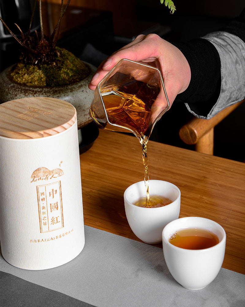 A person pouring Zen Tea Master Chinese Black Tea 130g into cups on a table.