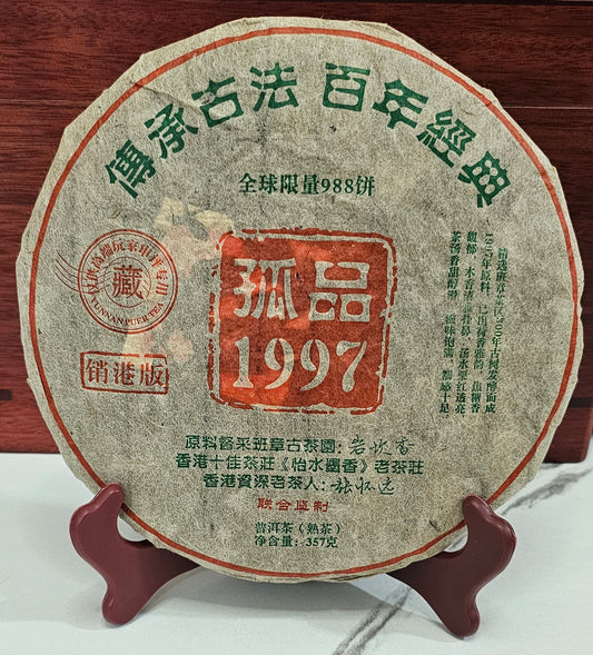 A circular, compressed tea cake with Chinese text, the number 1997 in red, displayed on a wooden stand against a red wood background.