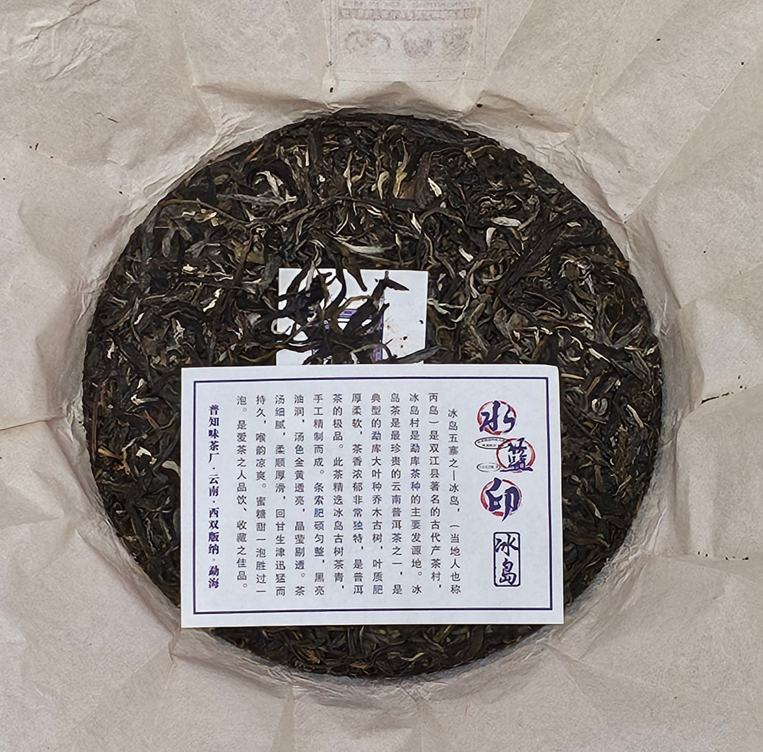 A round block of compressed tea leaves is wrapped in white parchment paper, featuring a label with Chinese text and symbols on top.