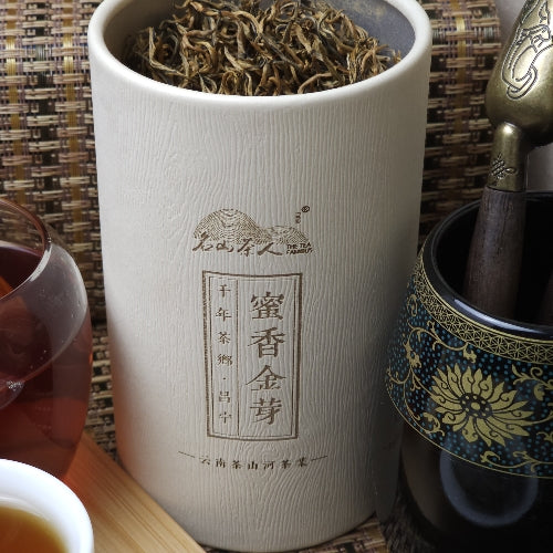 A cylindrical container filled with tea leaves next to a cup of tea and an ornate tea utensil. The container has Chinese characters inscribed on it.