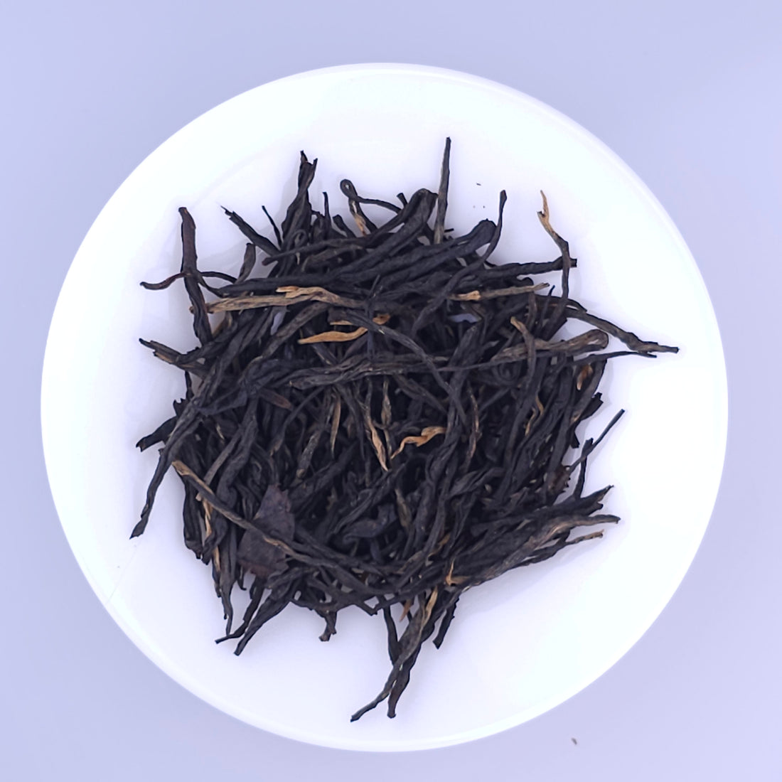 A white plate filled with dried dark tea leaves on a light background.