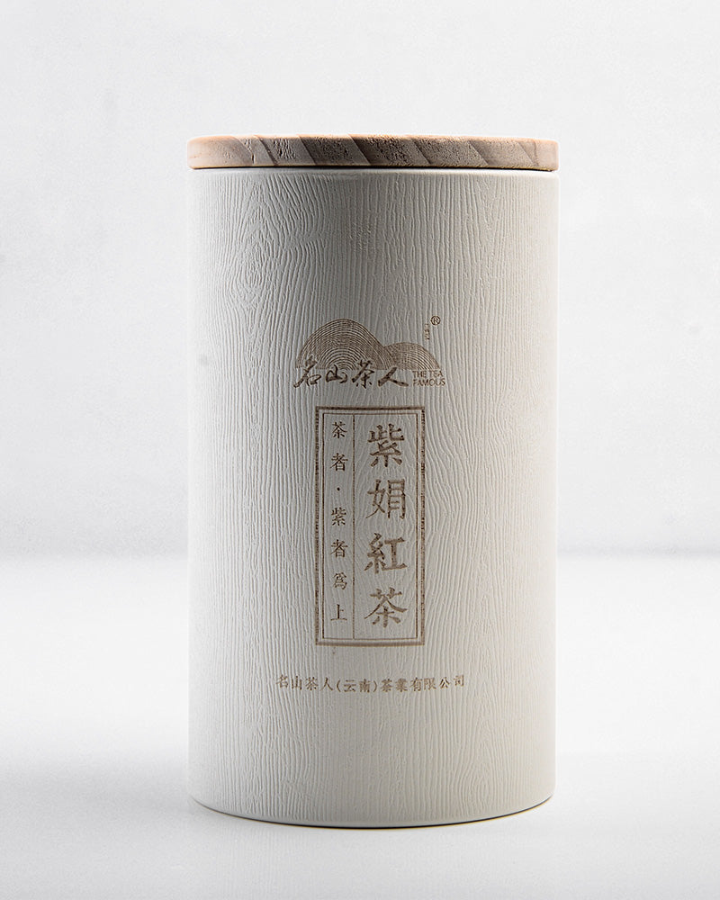 A cylindrical container with Asian script, featuring a white textured body and a wooden lid, stands upright against a plain background, housing Zen Tea Master's Zijuan Black Tea 130g/150g known for its high anthocyanin content.