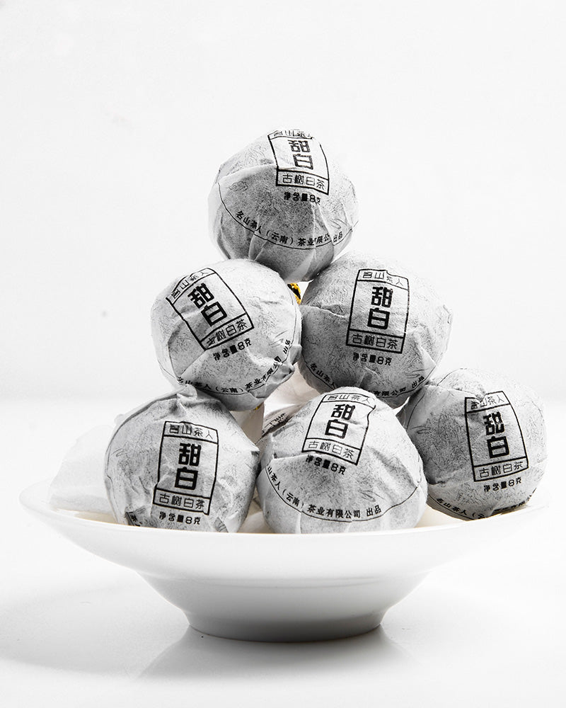 A stack of six wrapped Sweet White Antique Tree Beads 8g/80g by ZenTea Manor-YN001 arranged on a white plate against a plain background.