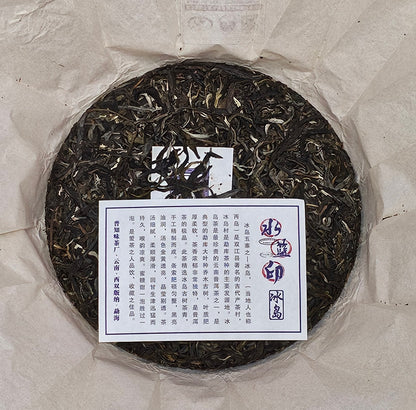 A round cake of white tea, evocative of the 2016 Bingdao Old Village (冰島老寨) - Water Blue Seal 88 Green Cakes (水藍印八八青餅) Pu-erh Raw Tea 357g from ZenTea Manor-YN005, is wrapped in paper with a label containing Chinese text placed on top, set against a neutral background.