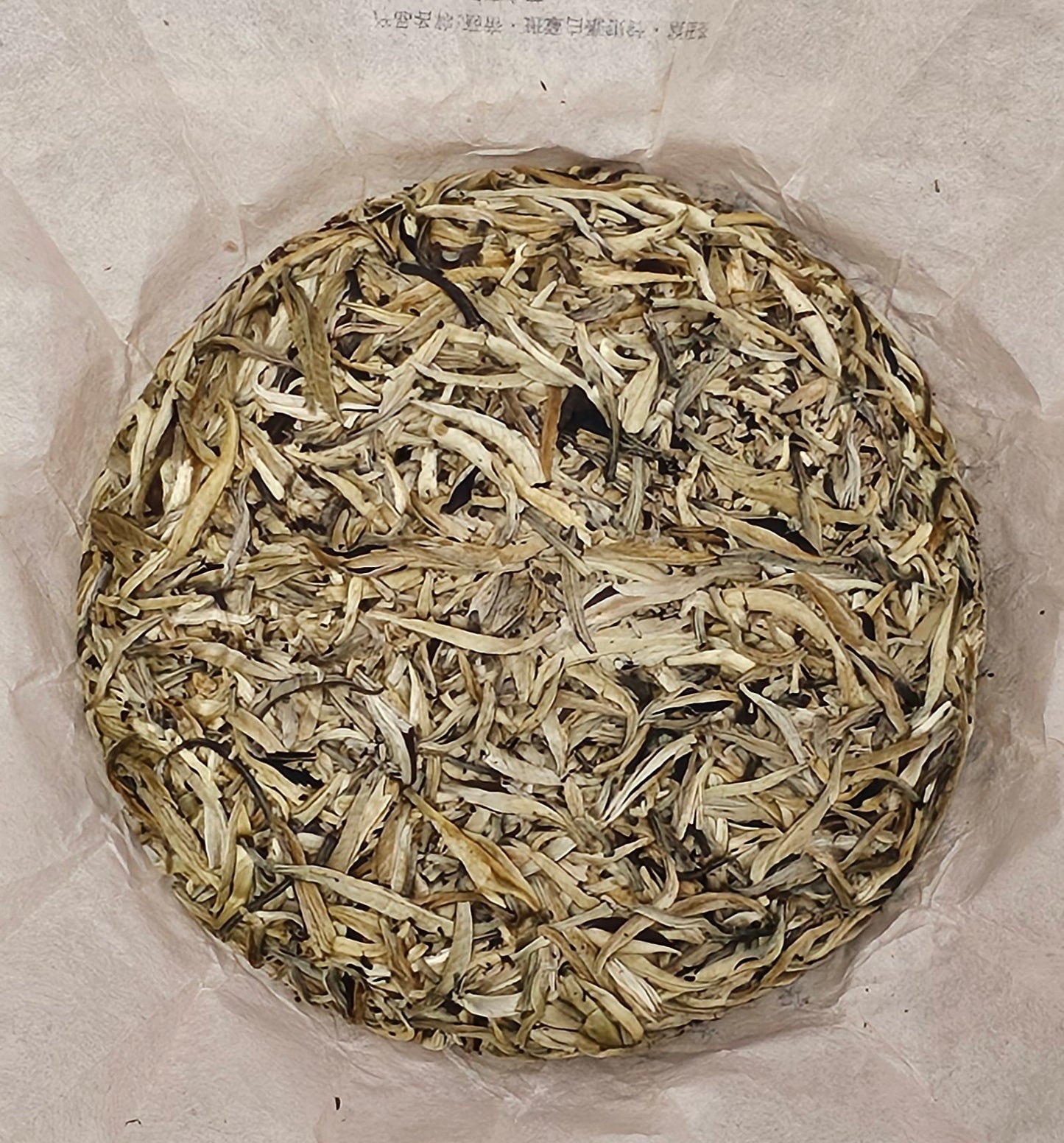 A circular arrangement of dried, light and dark tea leaves, including hints of ZenTea Manor-YN003 2002 Banzhang ( 班章 ) Tea King Ancient Tree ( 茶王古樹 ) White Hair Silver Needle White Tea ( 白毫銀針白茶 ) 357g, rests elegantly on parchment paper.