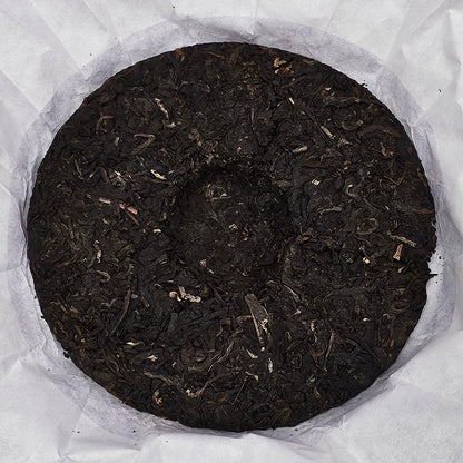 A round disc of compressed dark tea leaves, made from 2008 Jingmai Mountain (景邁山) Purple Tea (紫茶) 357g by ZenTea Manor-YN003, rests on a sheet of white paper.