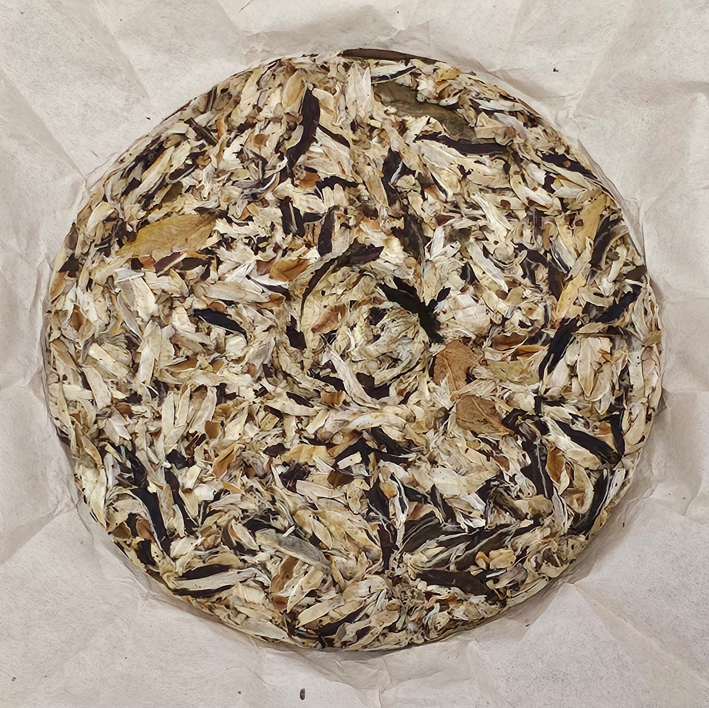 A round cake of ZenTea Manor-YN003 2005 Wild Ancient Tree Snow Bud Feather White Tea《野生古樹雪芽羽毛白茶》357g leaves and buds, wrapped in crinkled white parchment paper, sourced from the ancient tea trees of Xishuangbanna.