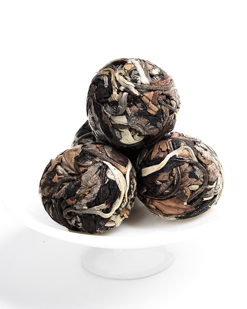 Four tightly rolled Sweet White Antique Tree Beads 8g/80g by ZenTea Manor-YN001 stacked on a white surface, offering a hint of wild flavor.