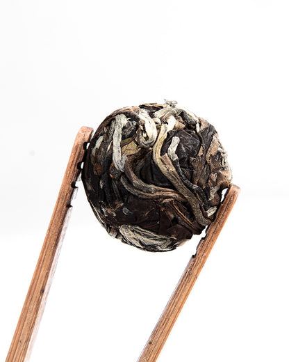 A pair of wooden chopsticks delicately holding a spherical ball of **Sweet White Antique Tree Beads 8g/80g** by **ZenTea Manor-YN001** against a white background.