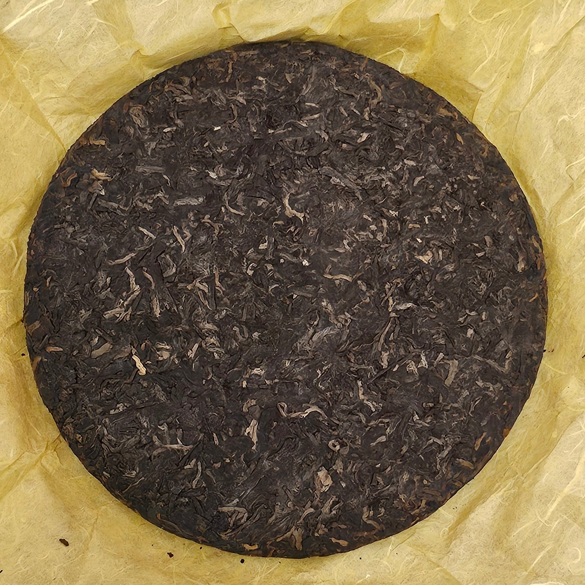 A round, compressed disk of **2008 Mansong Prince Mountain Tribute Tea ( 曼松王子山貢茶 ) - Wujin No.1 ( 烏金壹號 ) Puerh Ripe Tea 357g by ZenTea Manor-YN005** on a yellow crinkled paper.