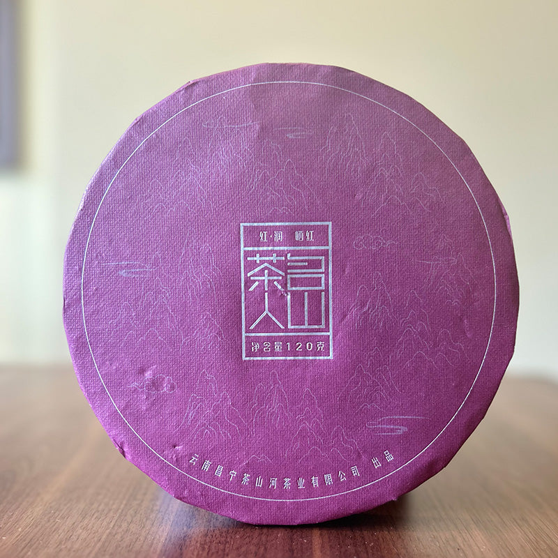 Circular package wrapped in purple paper with white Chinese characters and patterns, placed on a wooden surface, containing premium Rooibos Black Tea 120g from Zen Tea Master.