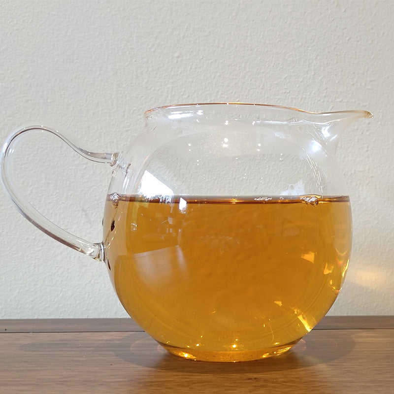 A glass pitcher filled with Sweet White Antique Tree Beads 8g/80g tea from Zen Tea Master, known for its fresh and elegant flavor, on a wooden table.