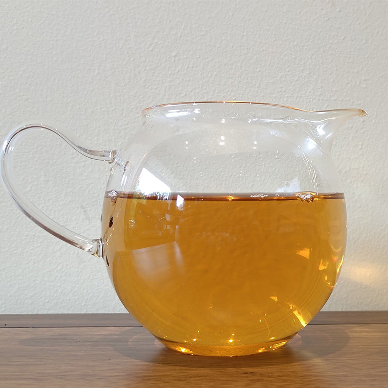 A clear glass pitcher filled with amber-colored Sweet White Antique Tree Beads 8g/80g by ZenTea Manor-YN001 sits on a wooden surface with a plain white background.