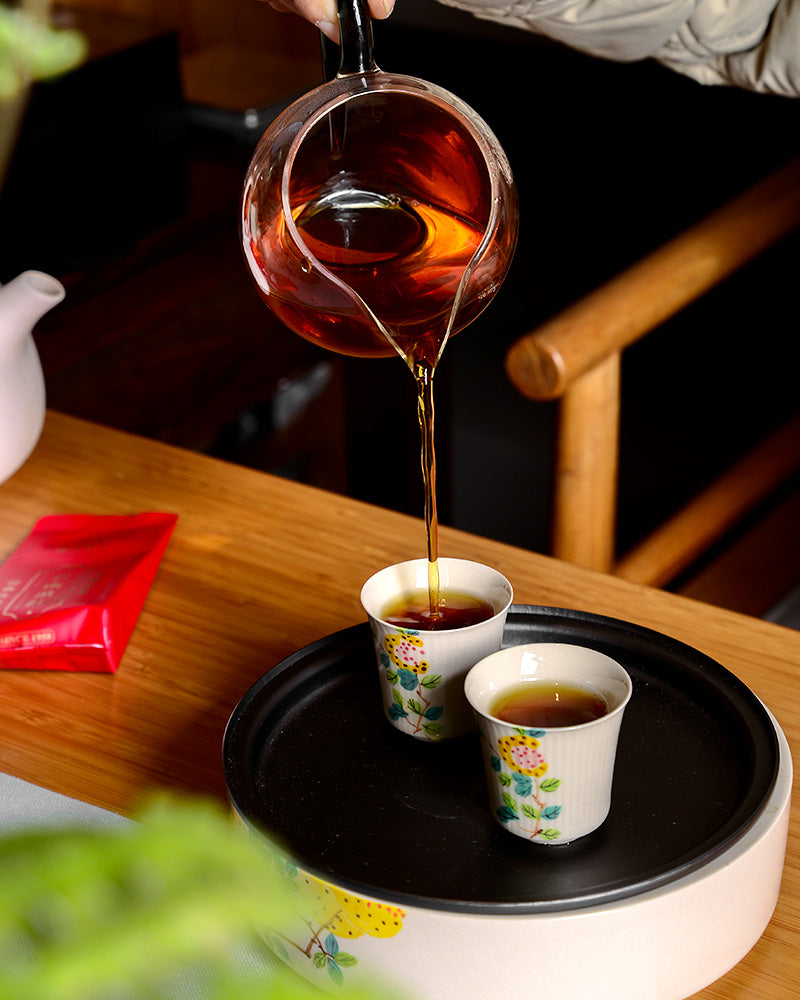 An expert pourer carefully prepares Classic Yunnan Red Bag tea using traditional black tea processing techniques, ensuring its exceptional quality and flavor. The perfectly brewed tea is then poured into cups arranged elegantly on Zen Tea Master.