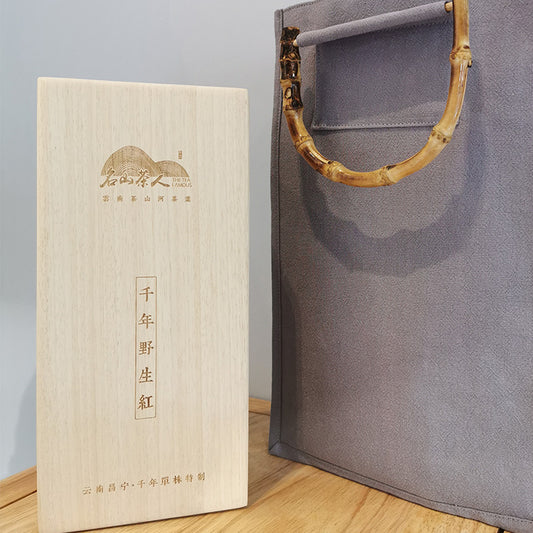 A wooden box with a bamboo handle next to it containing Millennium Wild Red Tea, also known as Dian Hong Tea - a top black tea by Zen Tea Master.